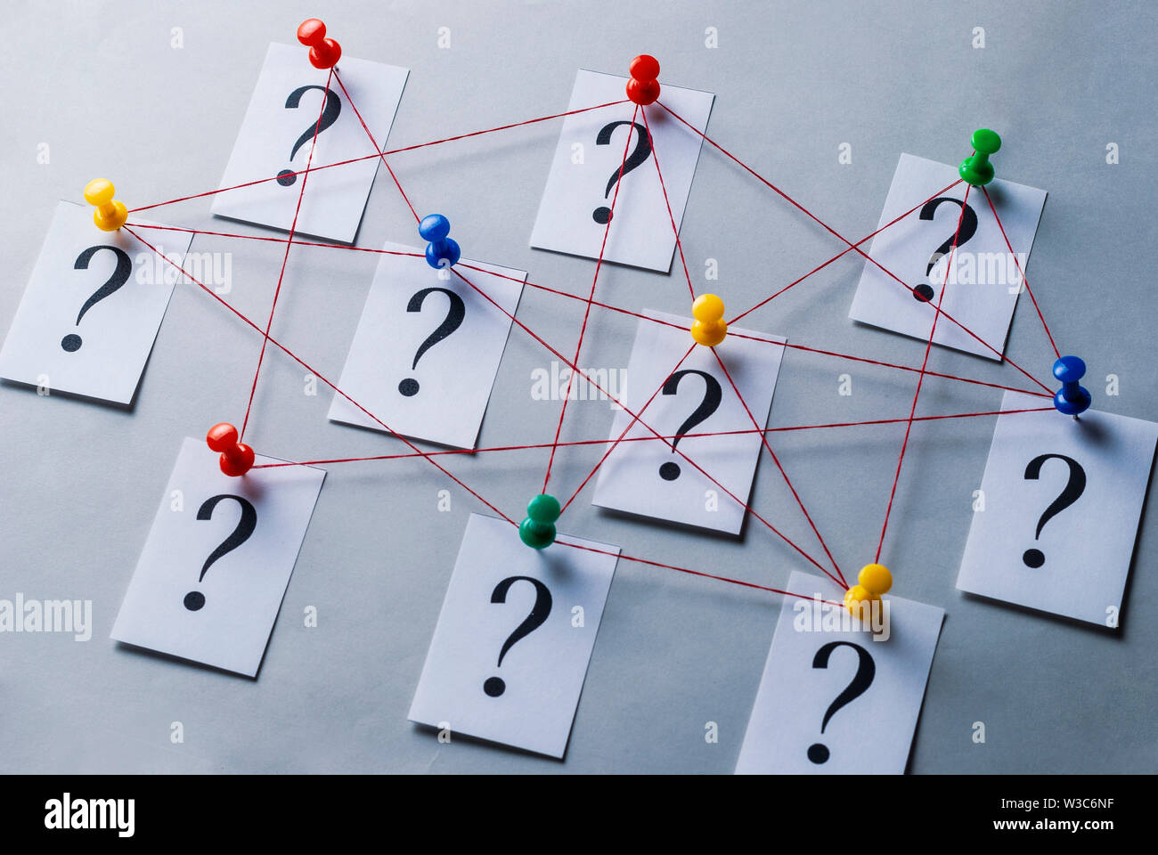 Réseau de points d'interrogation imprimés sur cartes blanches épinglées avec punaises et rejoint par chaîne dans un cadre conceptuel de l'image sur fond gris Banque D'Images