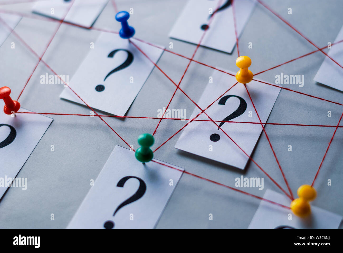 Réseau de points d'interrogation imprimés sur cartes blanches épinglées avec punaises et rejoint par chaîne dans un cadre conceptuel de l'image sur fond gris Banque D'Images