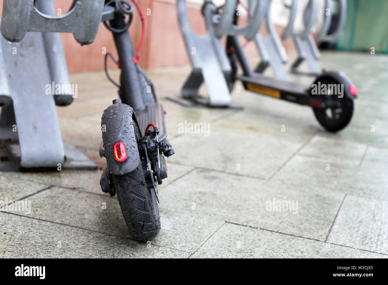 Des scooters électriques sur un parking lors d'une pluie, gouttes d'eau sur une des roues. Le temps pluvieux dans une ville, système de location de vélos Banque D'Images