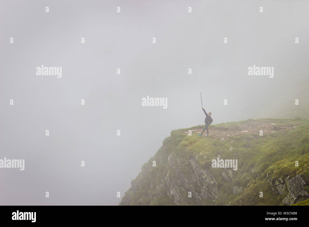 Fille randonneur avec bâton de marche et part dans l'air debout dans le brouillard au bord de la falaise sur la montagne de Rila en Bulgarie Banque D'Images