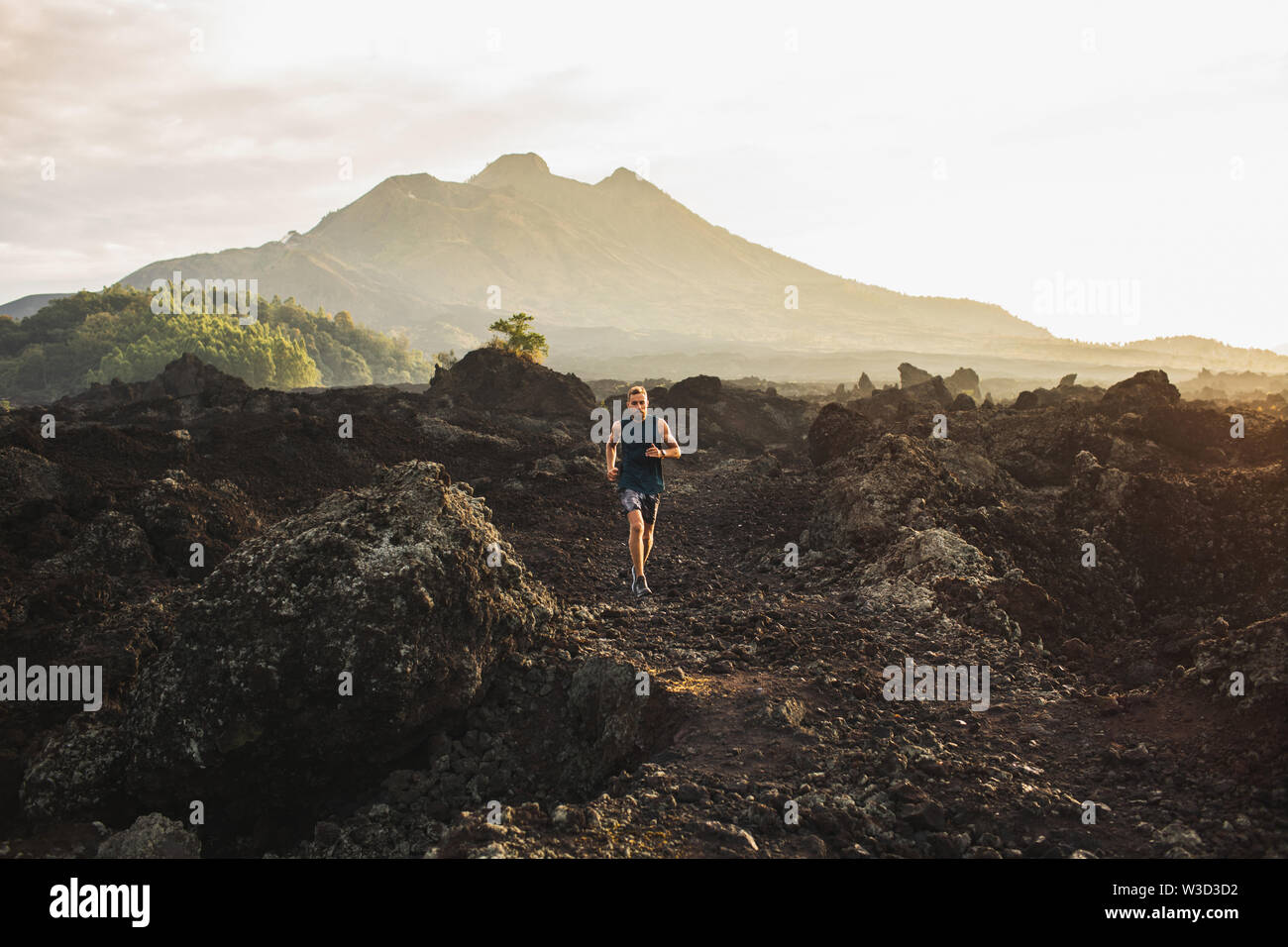 Jeune athlète homme trail running en montagne le matin. Amazing paysage volcanique du mont Batur Bali sur l'arrière-plan. Concept de vie sain. Banque D'Images