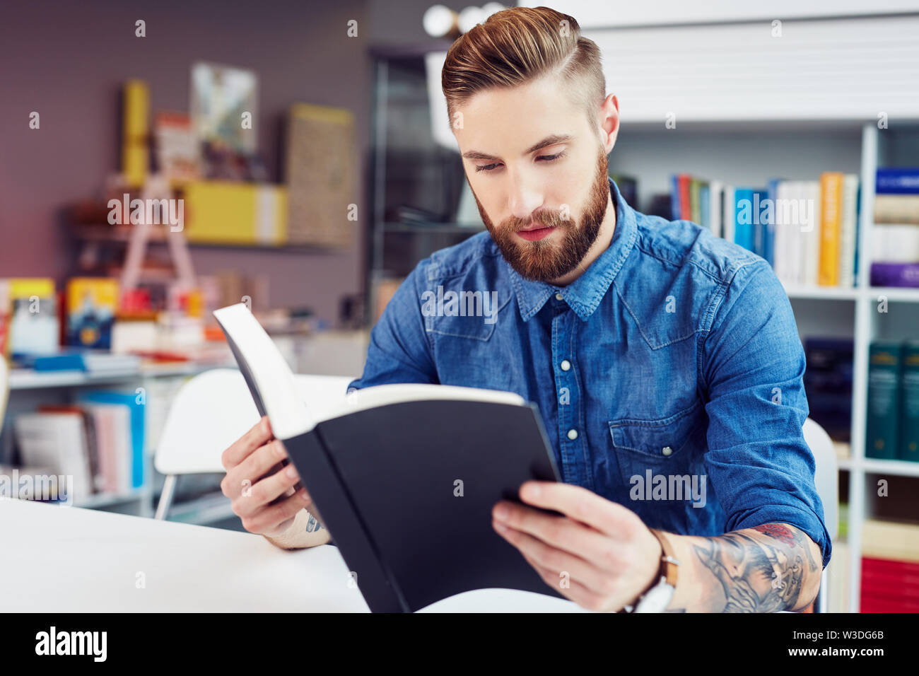Beau jeune homme student reading textbook en bibliothèque et l'étude Banque D'Images
