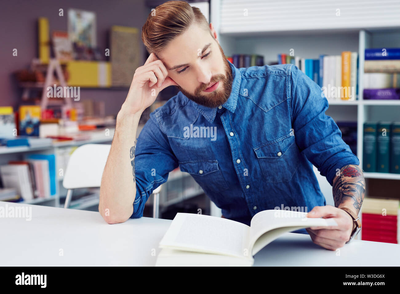 Souligné young male student reading textbook while sitting in library Banque D'Images