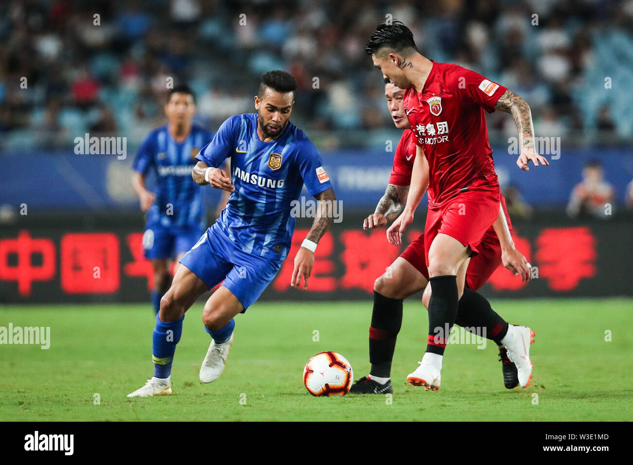 Joueur de football brésilien Alex Teixeira, gauche, de Jiangsu Suning passe le ballon contre des joueurs de la Shanghai EPOP dans leur 17e match au cours de l'Association de football chinoise 2019 Super League (CSL) dans la ville de Nanjing, Jiangsu province de Chine orientale, le 13 juillet 2019. Epop Shanghai Jiangsu défait Suning 3-0. Banque D'Images