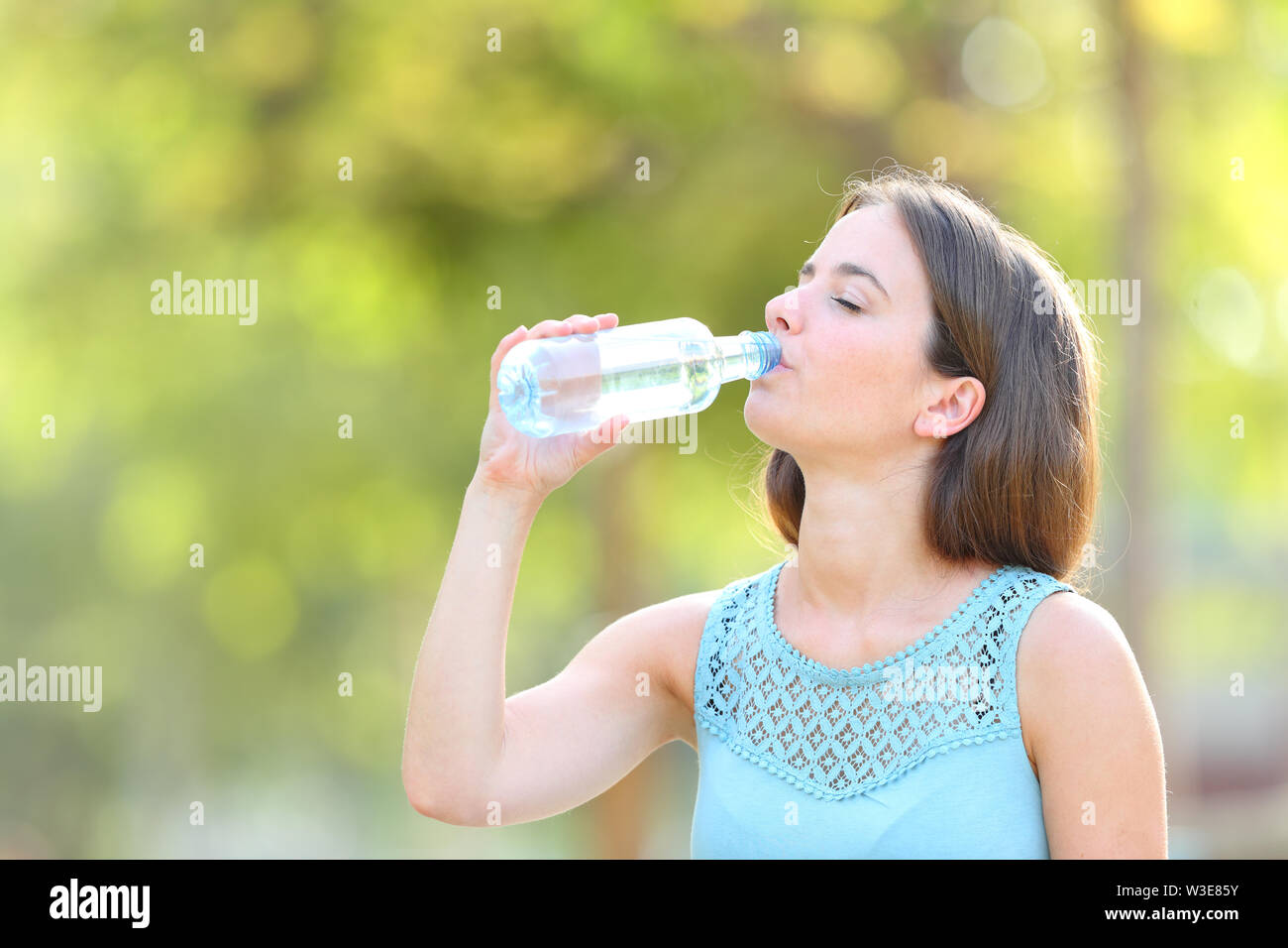 Femme de boire de l'eau en bouteille debout dans un parc Banque D'Images