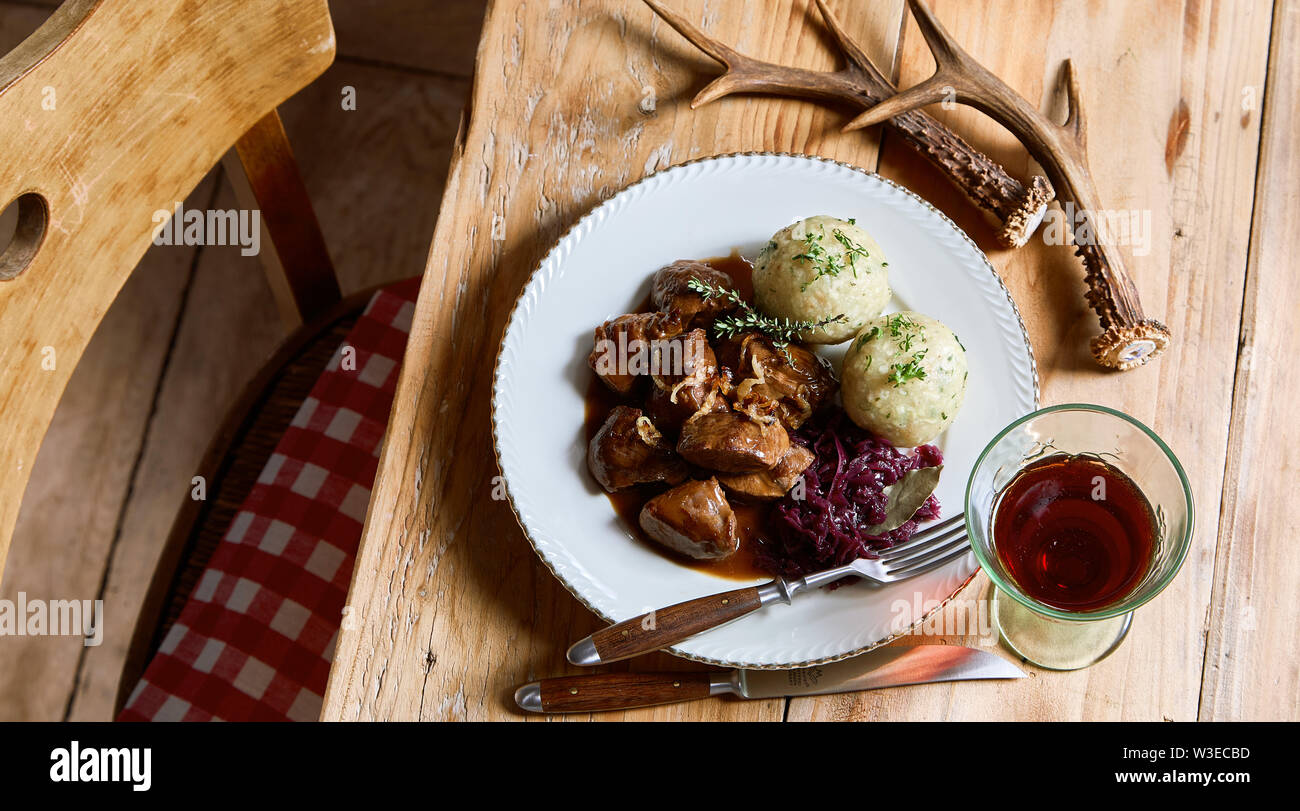 Servant de gibier sauvage goulasch et quenelles avec du chou rouge râpé et un verre de vin rouge sur un set de table rustique avec bois de cerf considéré un haut Banque D'Images