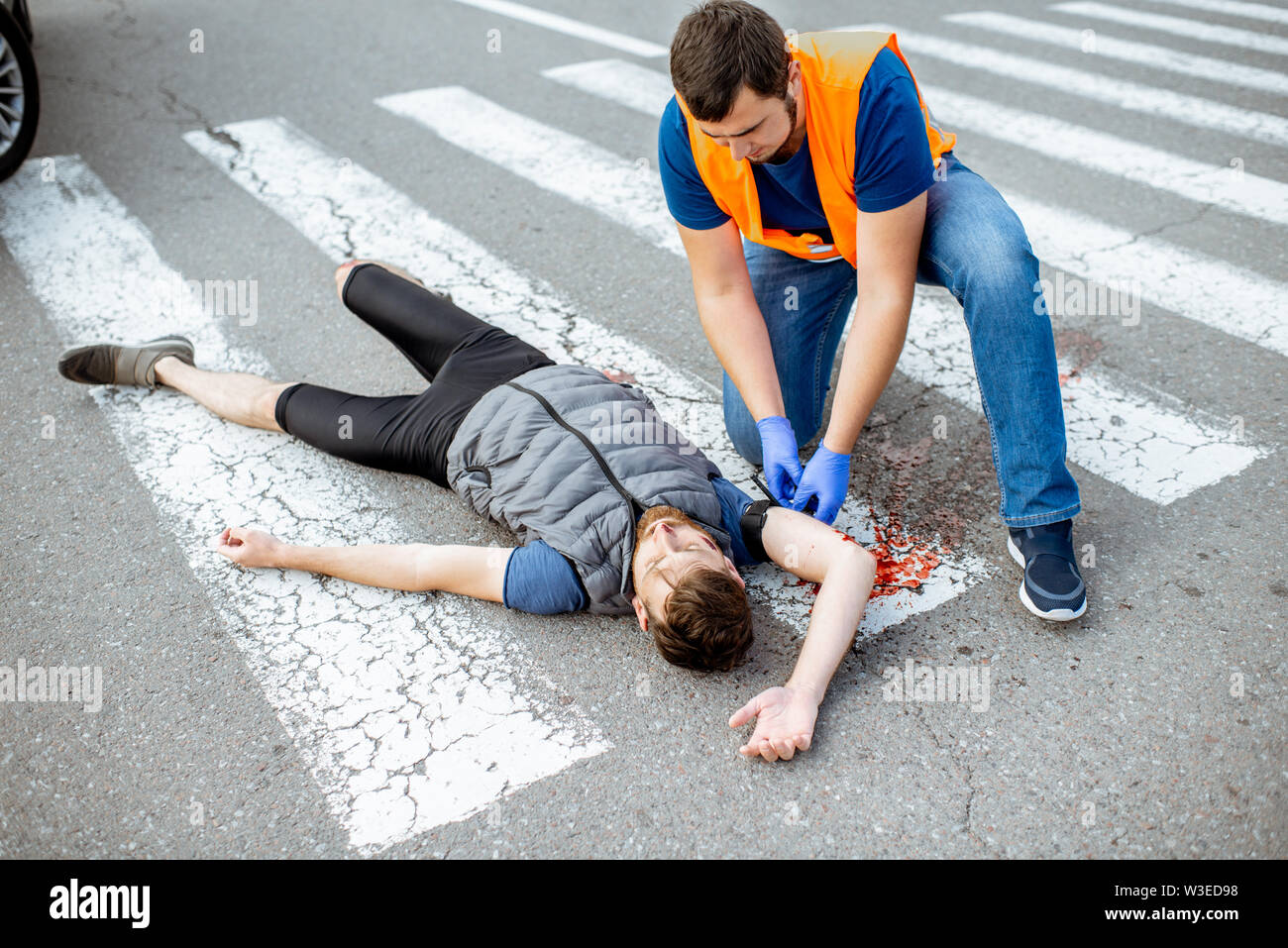 L'homme l'application de premiers secours aux blessés, personne purge garrot portant sur le bras après l'accident de la route sur le passage pour piétons Banque D'Images