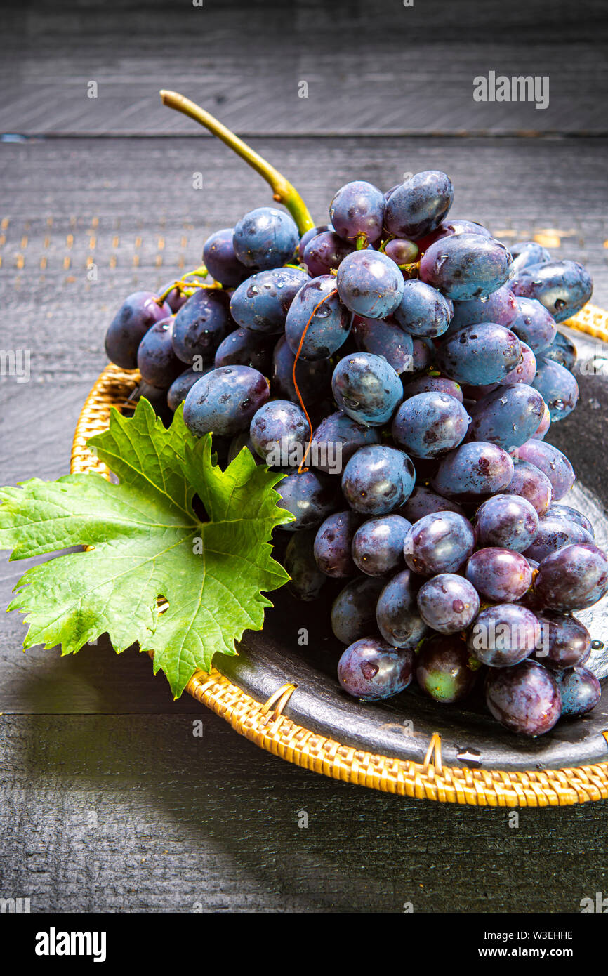 Bande de couleur bleu-noir à maturité des raisins de table avec feuille servi sur la plaque noire sur fond de bois noir Banque D'Images