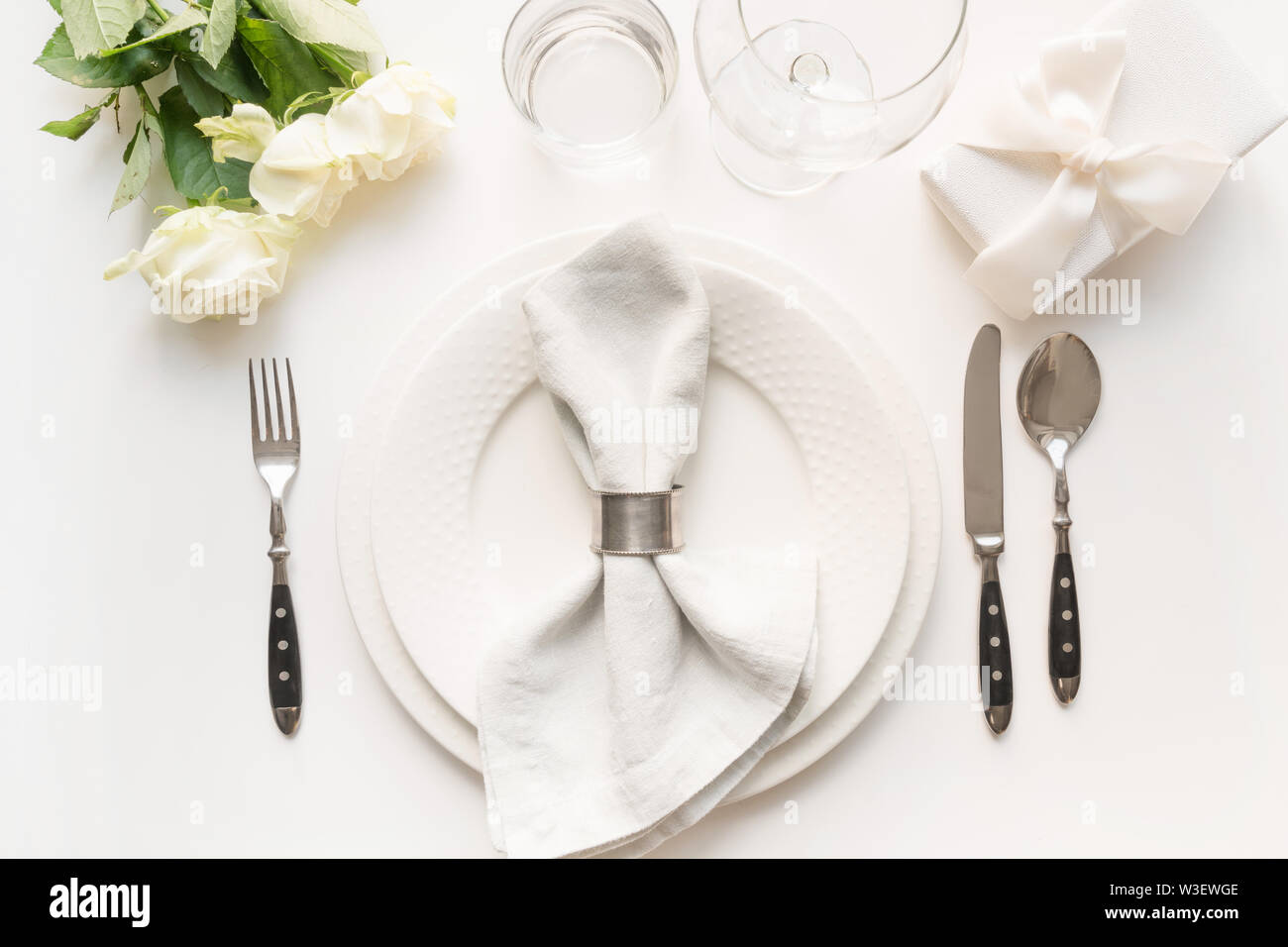 Tableau blanc avec bouquet rose, cadeau, vaisselle, couverts de table blanc en vacances. Vue d'en haut. Anniversaire de mariage et romantique. Banque D'Images