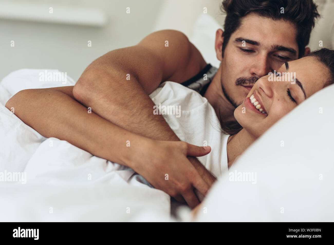 Beautiful happy young couple hugging tout en dormant sur le lit. Young man and woman lying together in bed. Banque D'Images