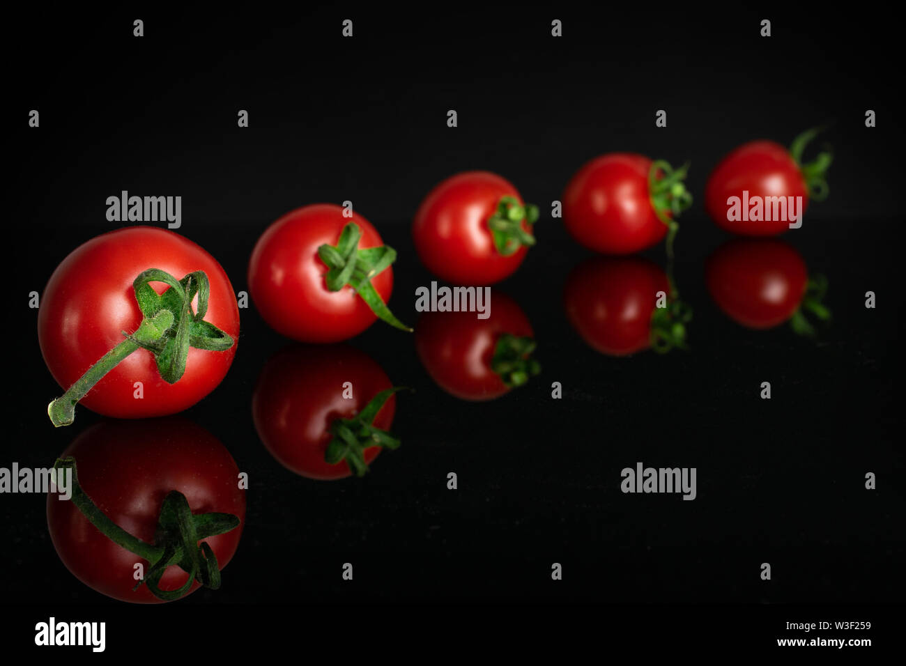 Groupe de cinq entiers et frais, tomate cherry rouge isolé sur verre noir Banque D'Images