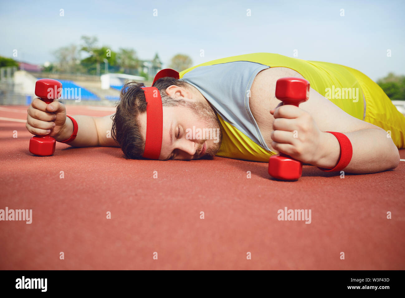 Fat lazy man sleeps fatigué se trouve sur la piste dans le stade. La notion de perte de poids, le régime alimentaire. Banque D'Images