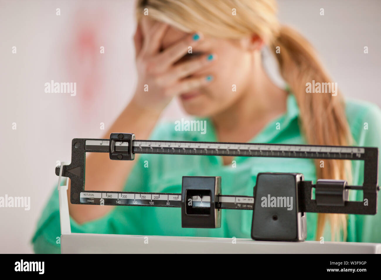 Jeune femme couvrant ses yeux avec désespoir tandis qu'à l'aide d'une balance médicale. Banque D'Images