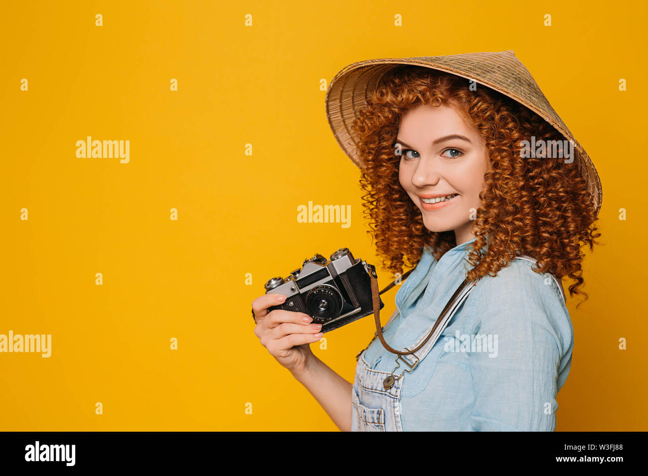 Cute traveler en chapeau chinois avec appareil photo rétro sur fond jaune Banque D'Images