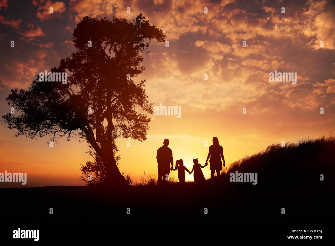 Famille heureuse silhouette debout sur contre l'heure du coucher du soleil. Banque D'Images