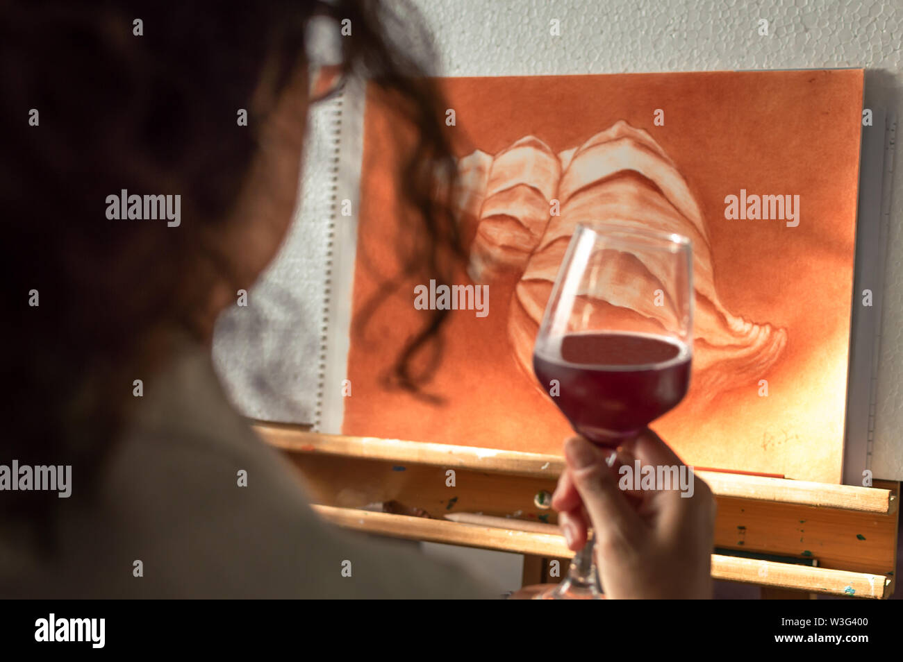 Femme buvant un verre de vin pour célébrer qu'elle a fini sa peinture. Artiste en contemplant son travail fini. Banque D'Images