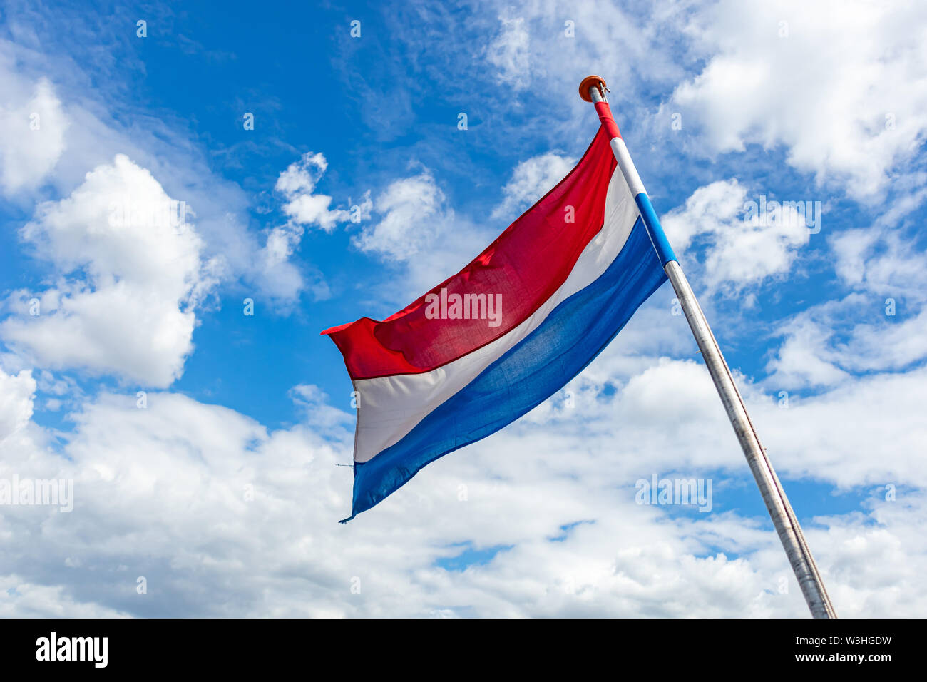 Drapeau des Pays-Bas. Symbole national néerlandais agitant sur perche contre ciel bleu avec des nuages, journée ensoleillée Banque D'Images