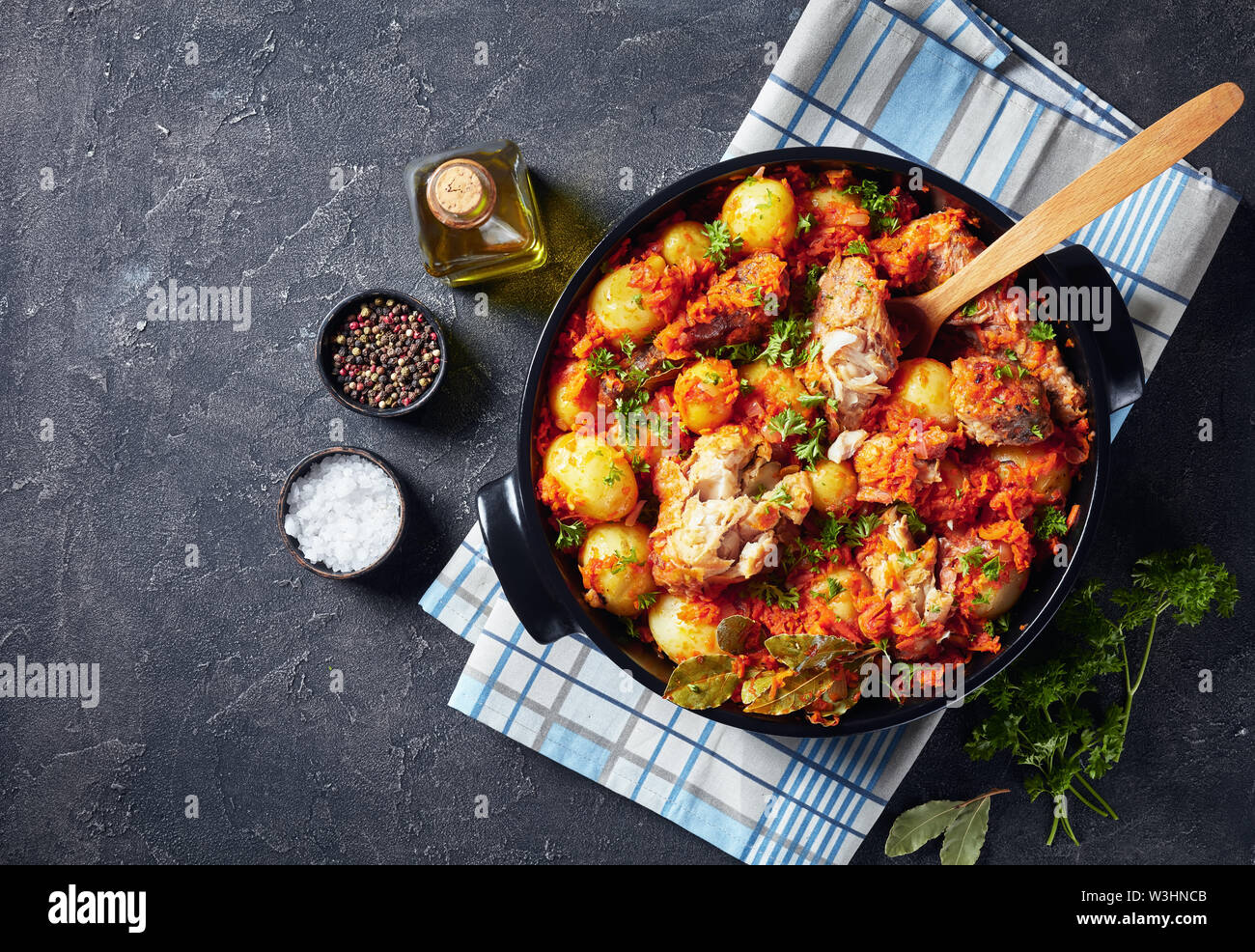 Vue aérienne de merlu braisé cuit avec des pommes de terre nouvelles et de légumes dans une casserole en céramique noire, vue de dessus, flatlay, close-up, copy space Banque D'Images