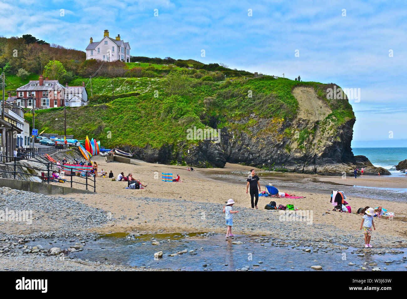 Les familles avec de jeunes enfants profiter de jouer dans l'eau sur la plage de l'anse abritée à Llangrannog. Collection colorée de planches de surf. Banque D'Images