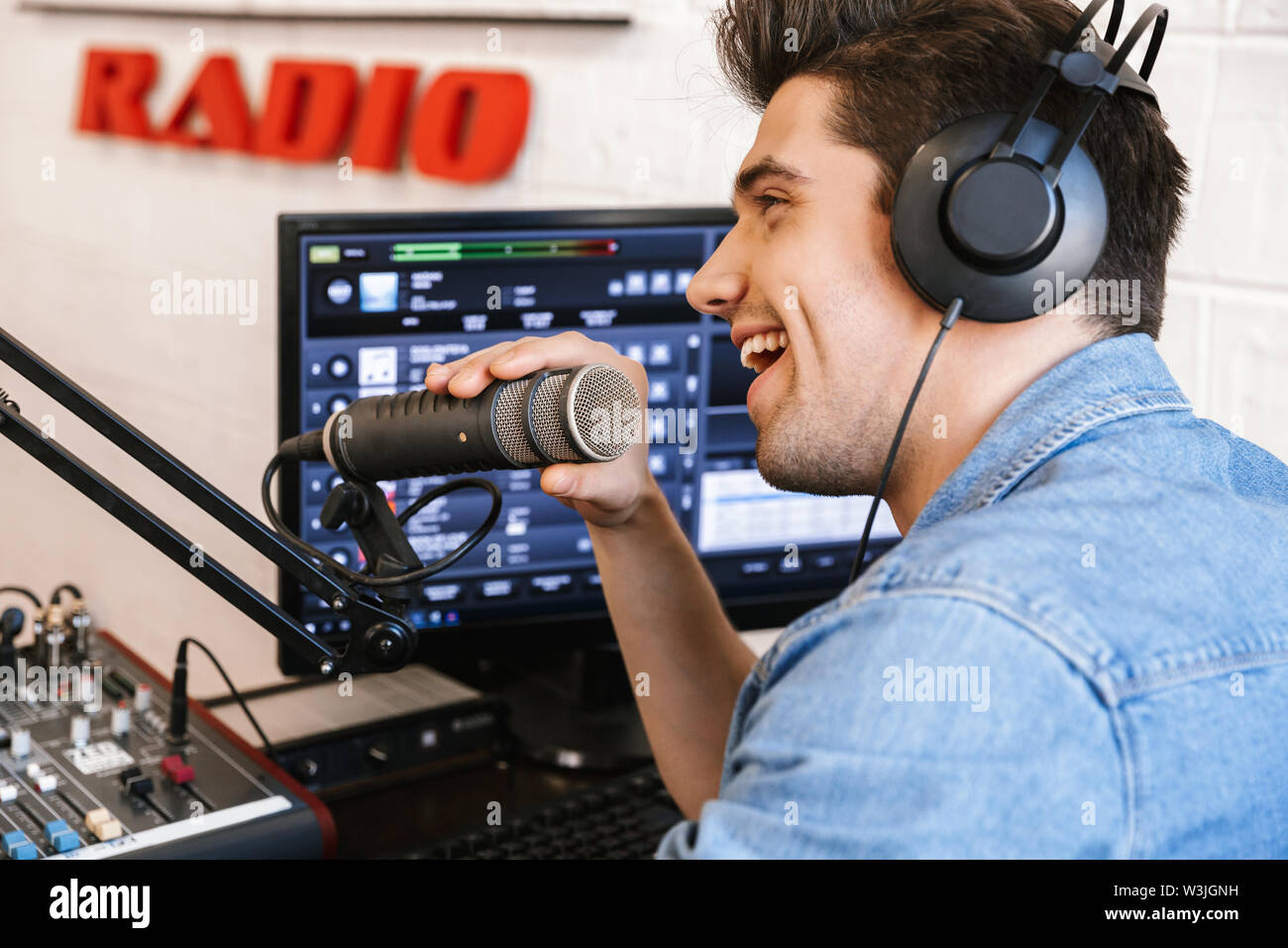 Beau jeune homme animateur de radio broadcasting en studio, à l'aide de microphone et casque Banque D'Images