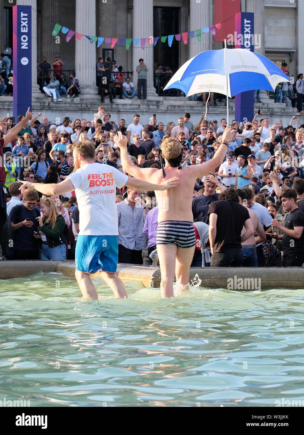 Deux fans de cricket danse pour célébrer la victoire en Coupe du Monde à Trafalgar Square's fontaines avec foule regardant en arrière-plan Banque D'Images