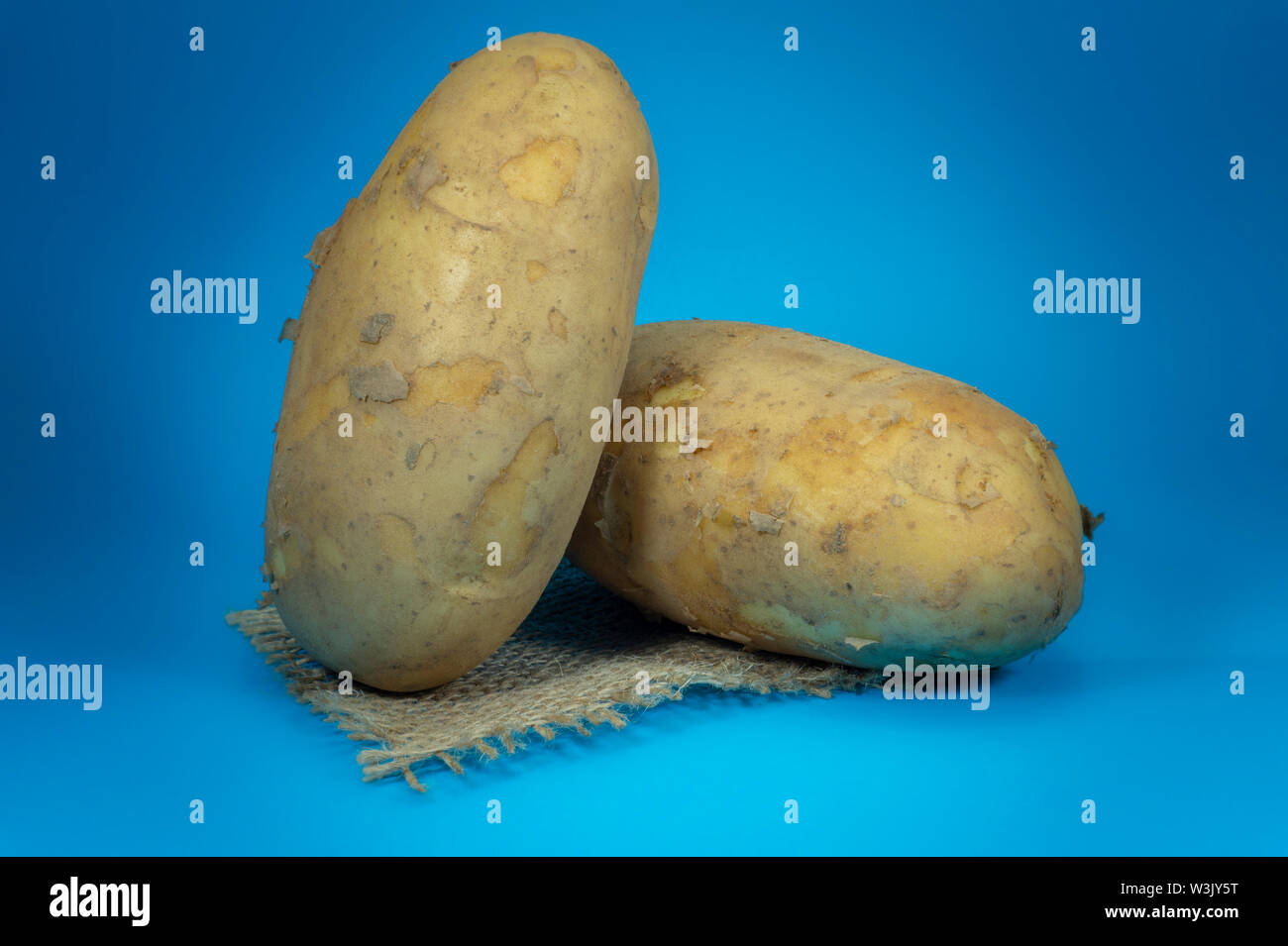 Matières, sans les laver, éplucher les pommes de terre sur un carré de jute isolé sur fond bleu Banque D'Images