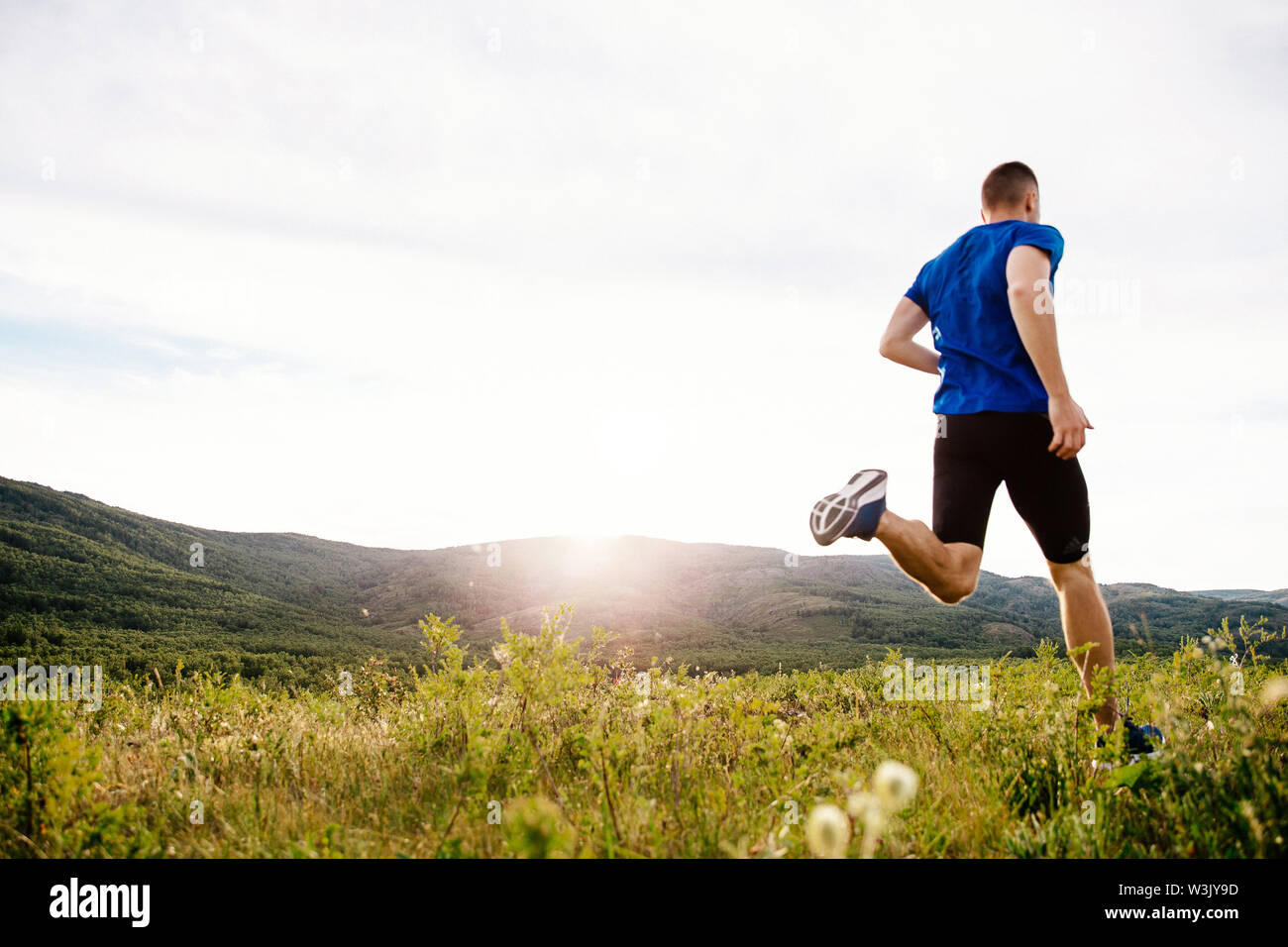 Retour homme runner s'exécutant sur le plateau d'été dans l'herbe motley coucher du soleil Banque D'Images
