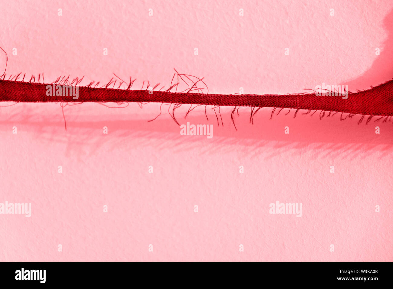 Une bande de tissu effiloché contre un mur , belle ombre du tissu sur l'arrière-plan avec de minces et fils verticaux Banque D'Images