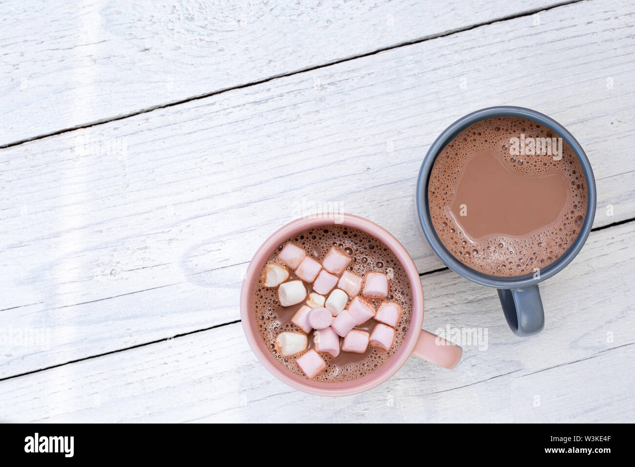 Chocolat chaud dans deux tasses, avec de petites guimauves, isolé sur le bois peint blanc à partir de ci-dessus. L'espace pour le texte. Banque D'Images