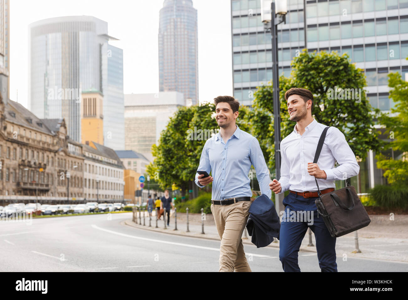 Photo d'un heureux jeune deux amis collègues hommes d'affaires la marche à l'extérieur à côté holding phone. Banque D'Images