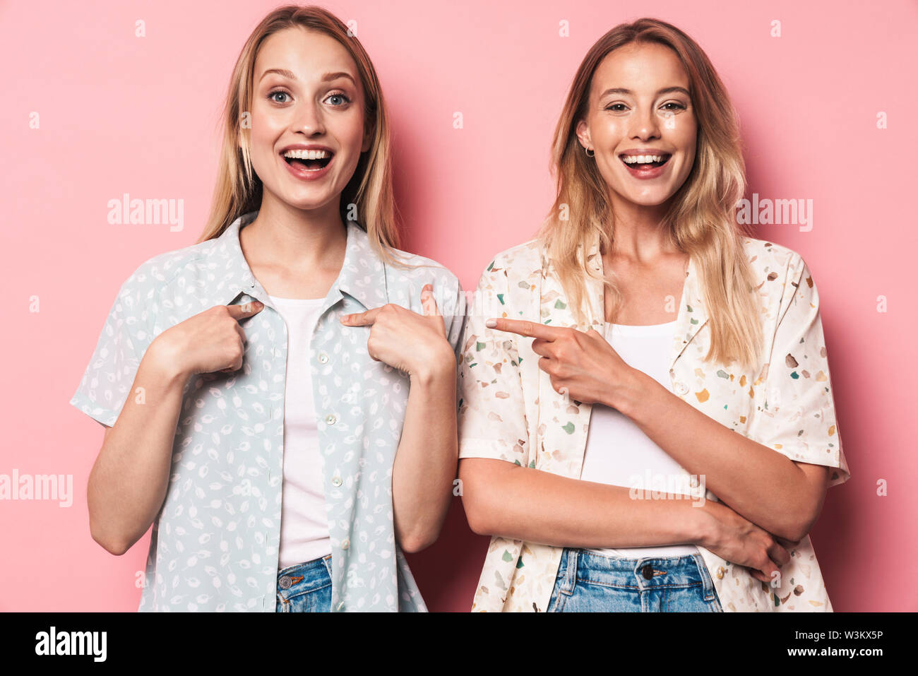 Deux young girls isolés sur fond rose, pointer du doigt Banque D'Images