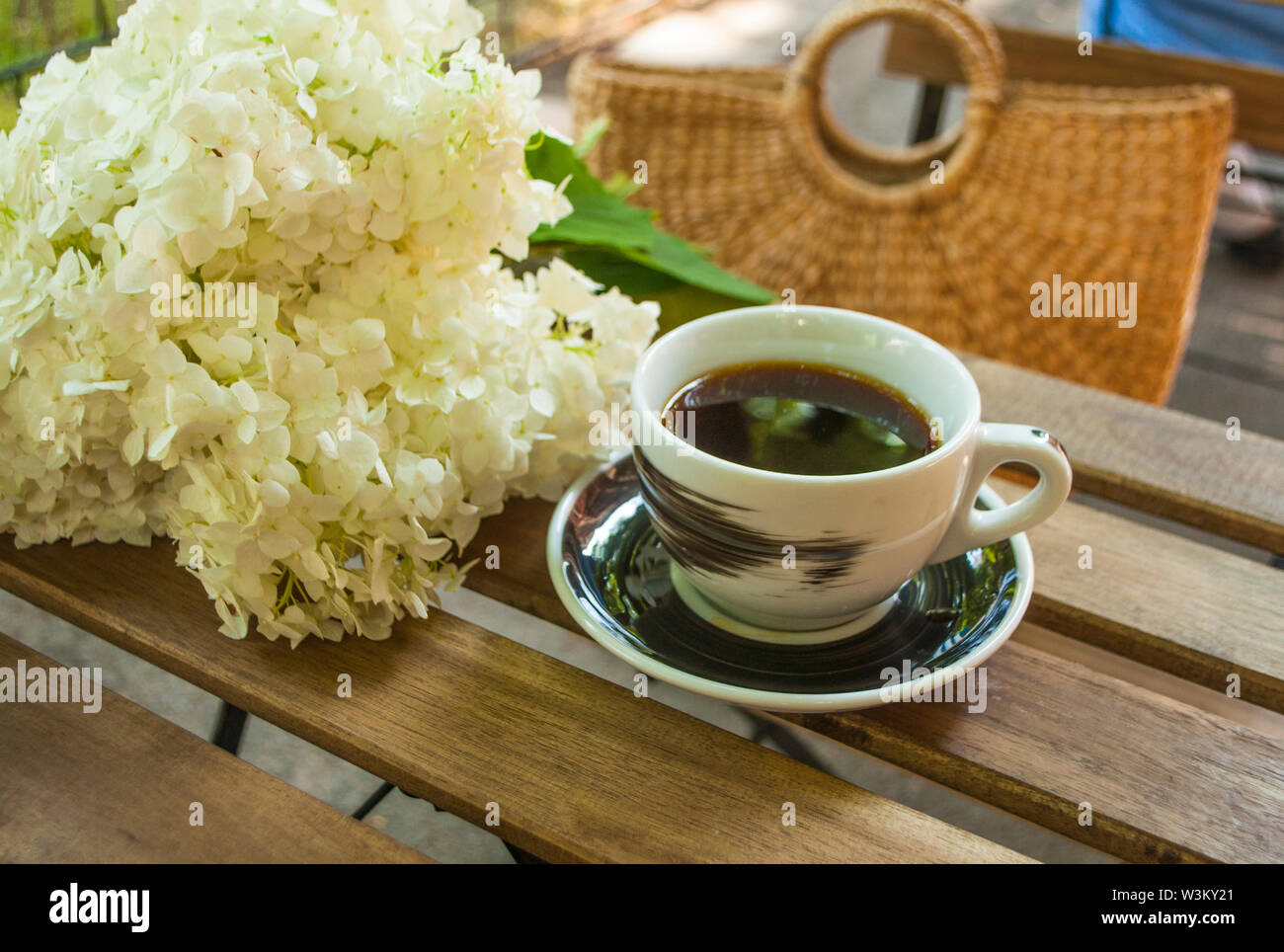 Une tasse de café noir sur une table en bois et un sac de paille avec hydragea fleurs sur l'arrière-plan. Banque D'Images