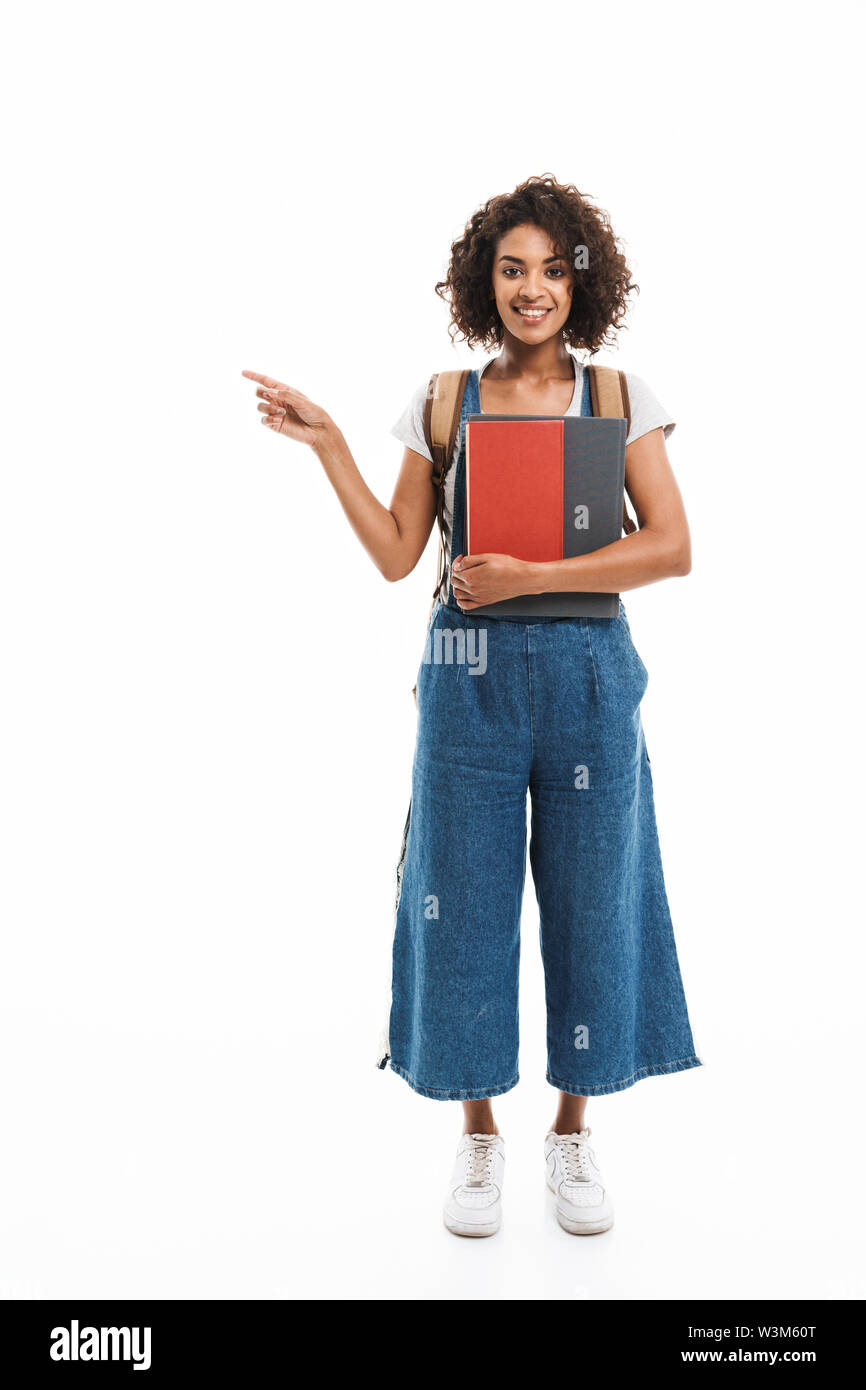 Image de plaisir african american woman wearing backpack doigt à copyspace et holding books isolé sur fond blanc Banque D'Images