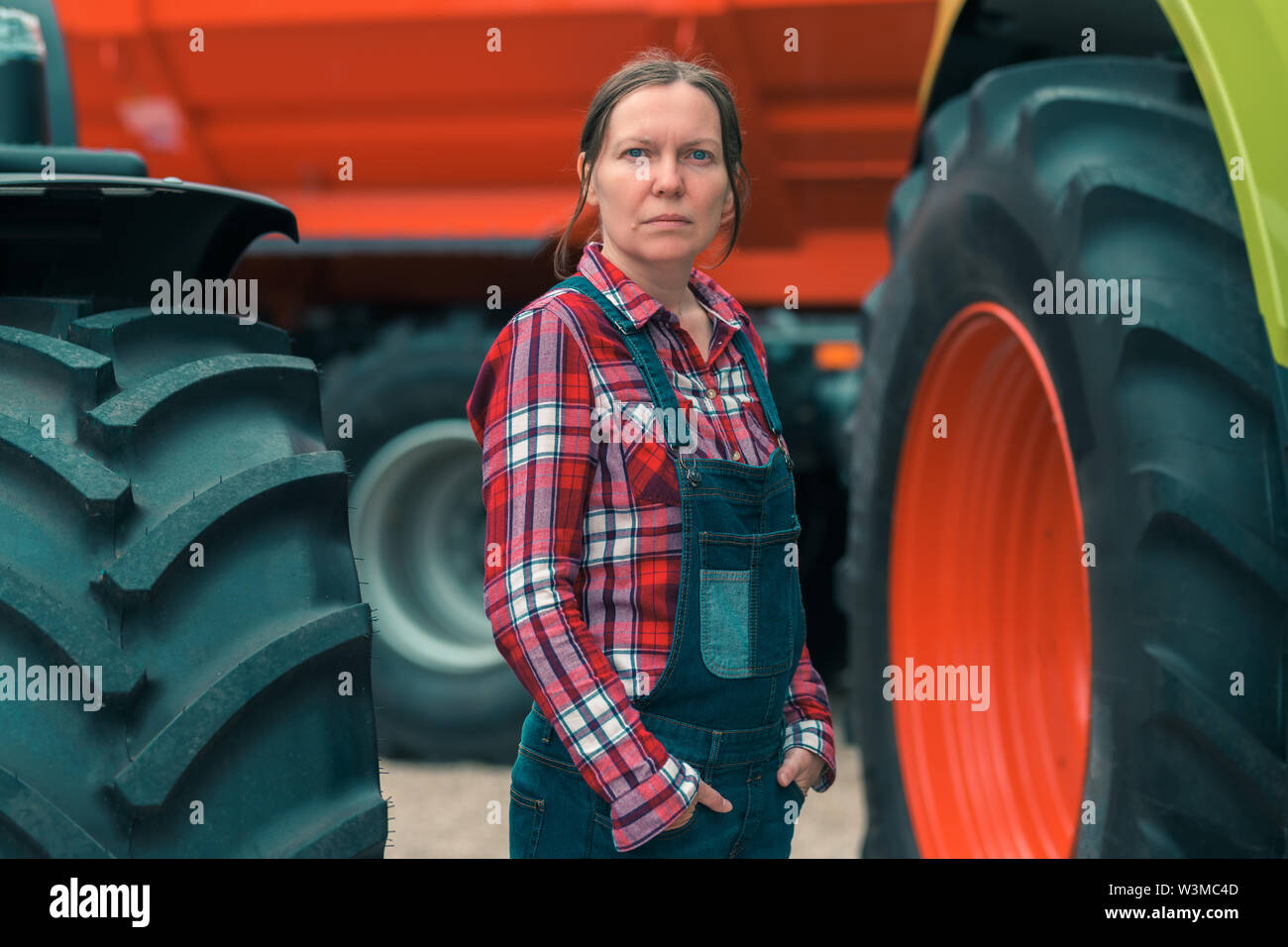 La productrice et le tracteur. Femme men's job concept. Travailleur agricole féminin posant devant des machines agricoles. Banque D'Images