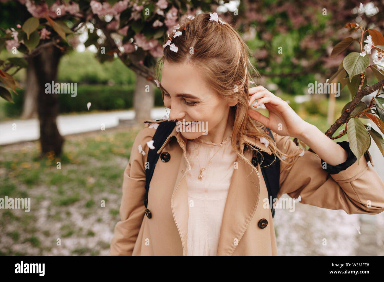 Femme souriante entre les pétales tombant d'un arbre en fleurs Banque D'Images