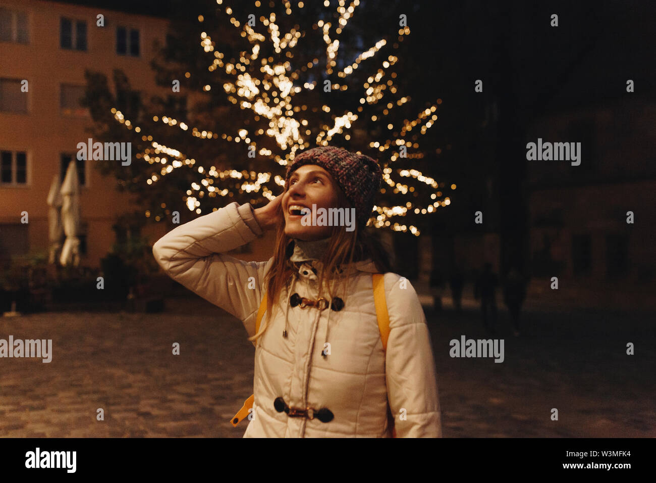 Smiling woman wearing coat par fairy lights in tree at night Banque D'Images
