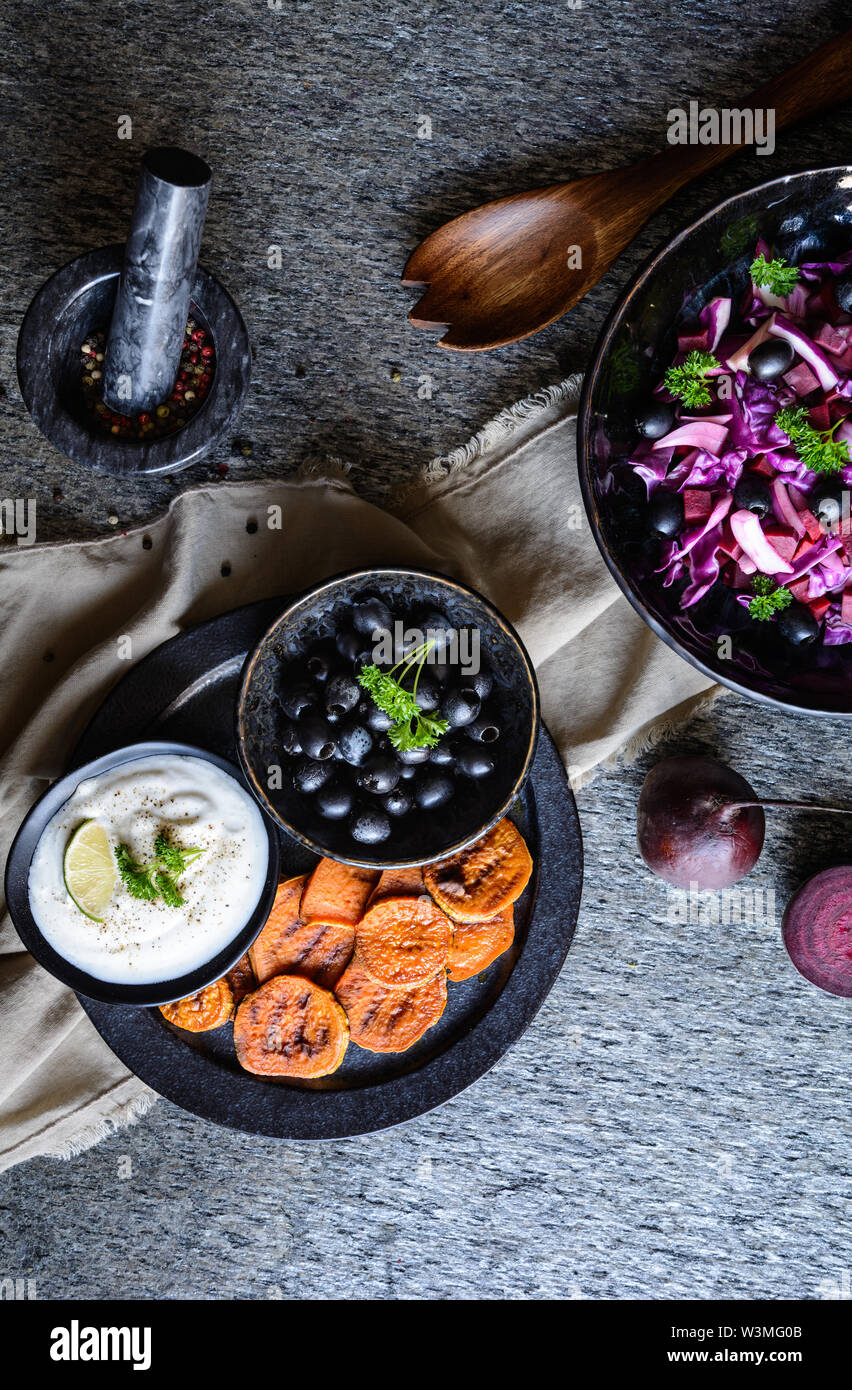 Tranches de pommes de terre frits servis avec trempette de crème sure, olives noires et salade faite de chou rouge, oignon rouge et betterave Banque D'Images
