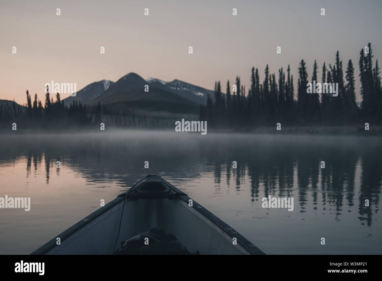 Un canot glisse sur l'eau calme d'une rivière alors que le ciel commence à briller doucement, peu avant le lever du soleil. Territoire du Yukon, Canada Banque D'Images