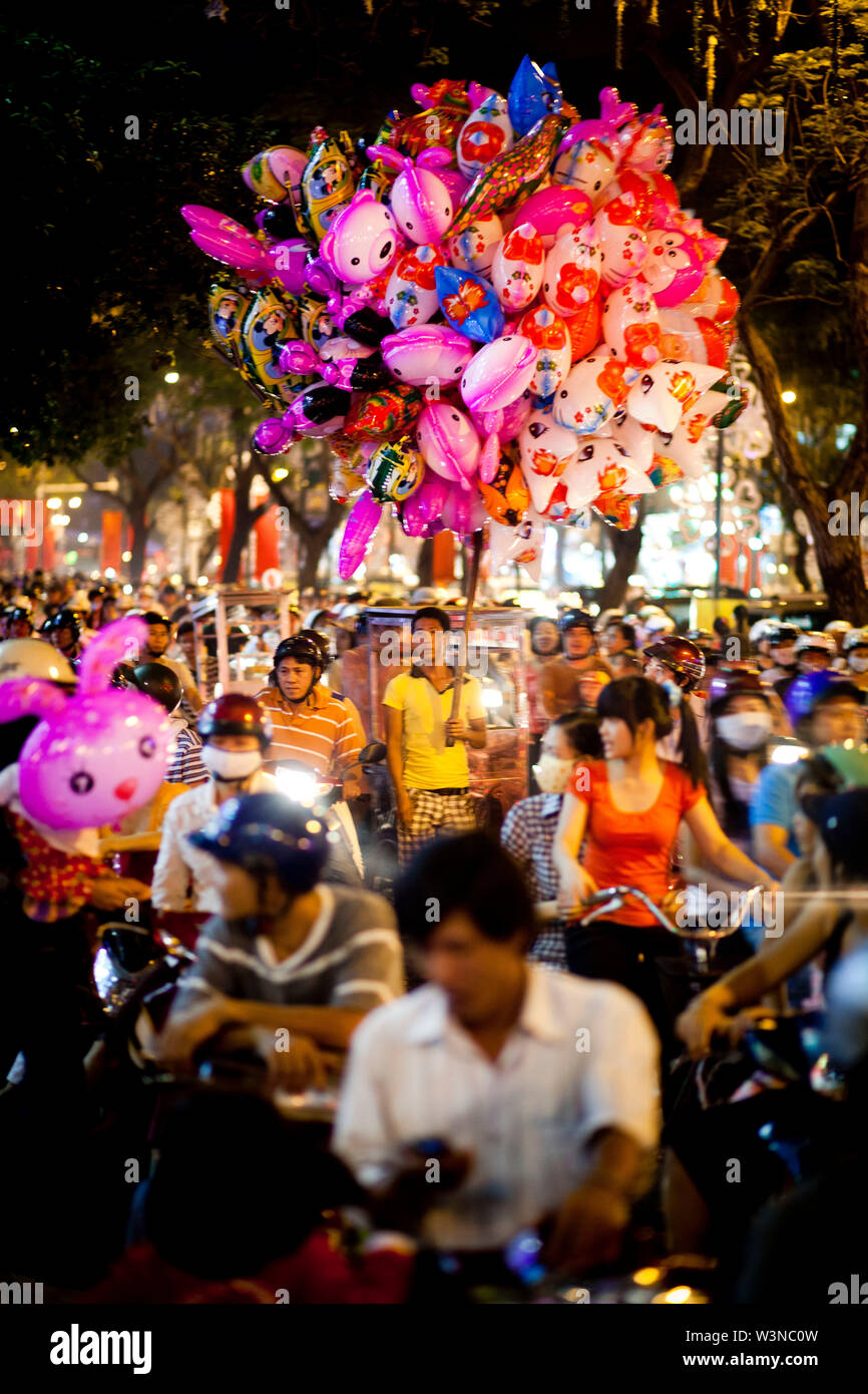 Un homme asiatique se dresse au milieu de la vente de ballons à la circulation nuit à Ho Chi Minh Ville au Vietnam du sud de l'Asie. Banque D'Images