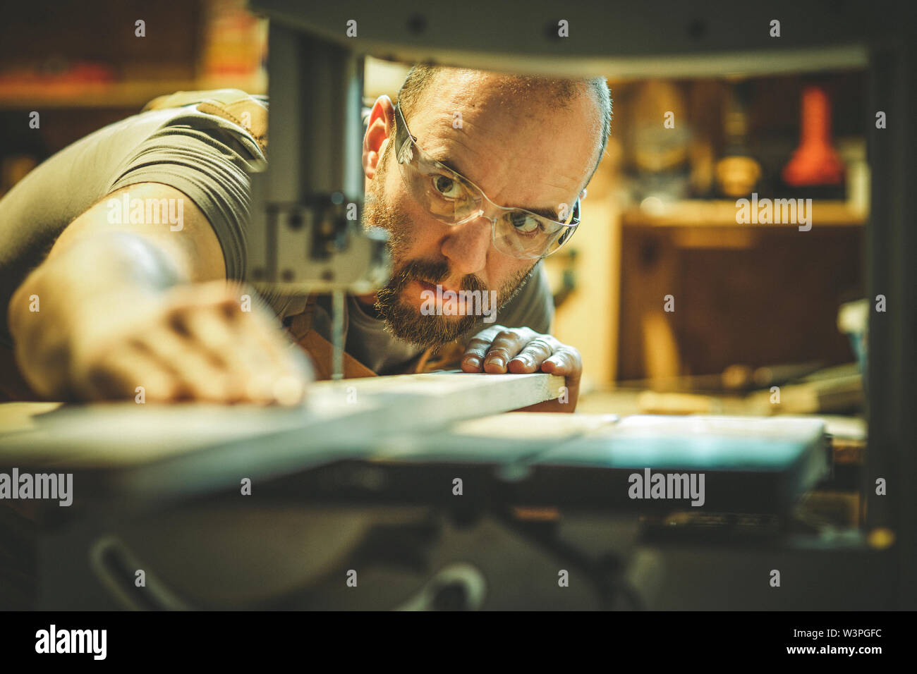 Détail d'un menuisier au travail une planche de découpe avec une scie à ruban dans son atelier, caucasien, avec une barbe et des lunettes. Banque D'Images