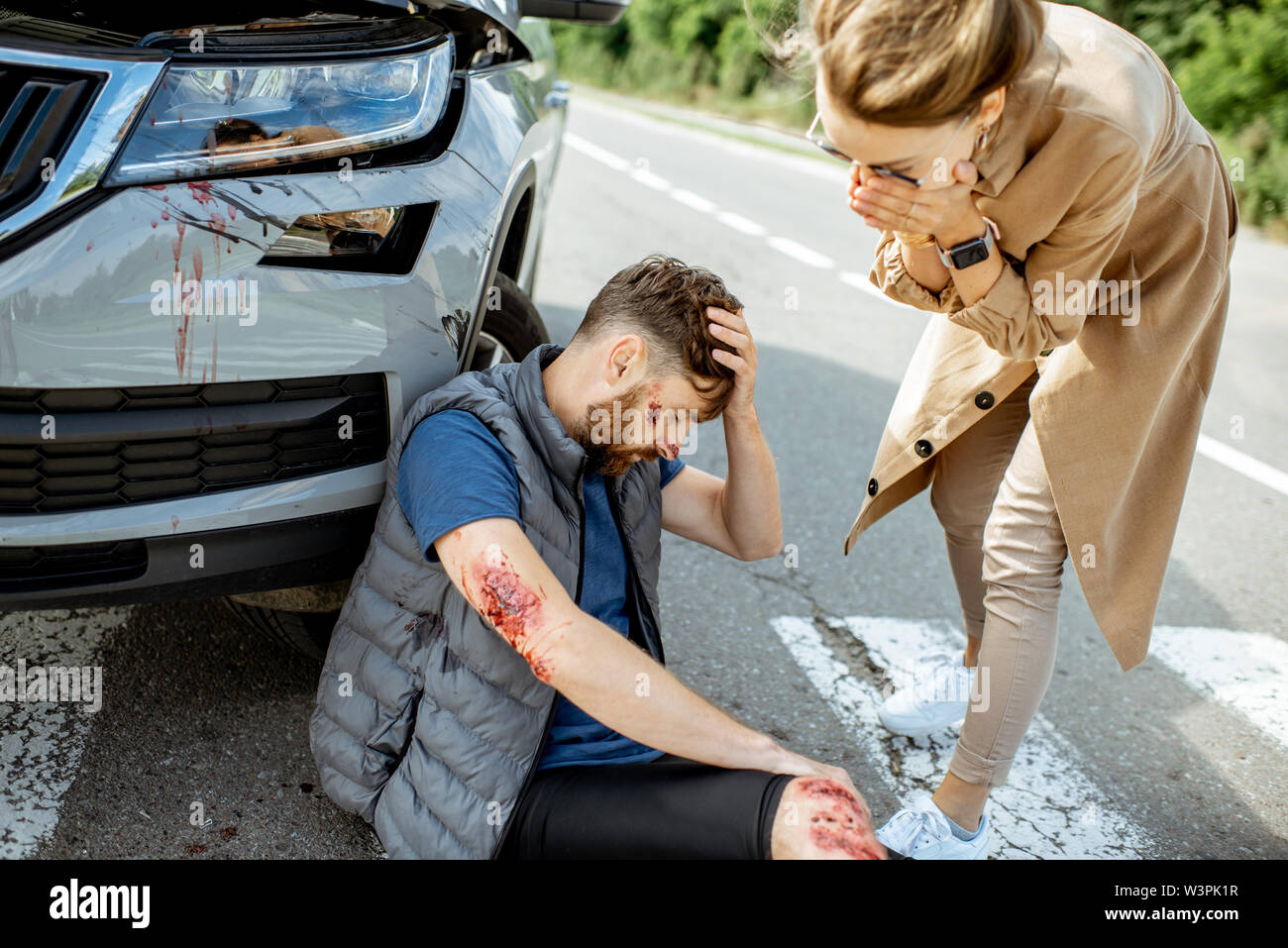 Femme m'apitoyer sur l'homme blessé de la souffrance sur le passage pour piétons près de la voiture après l'accident de la route Banque D'Images