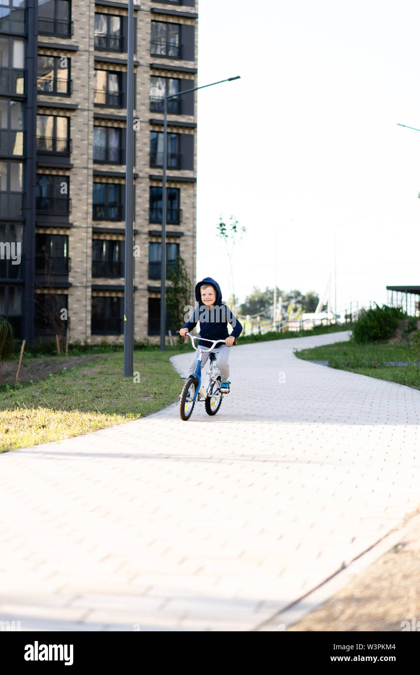 La sécurité dans une ville européenne moderne. Un petit garçon heureux monte un vélo à une cour fermée dans un bâtiment urbain à plusieurs étages. Banque D'Images