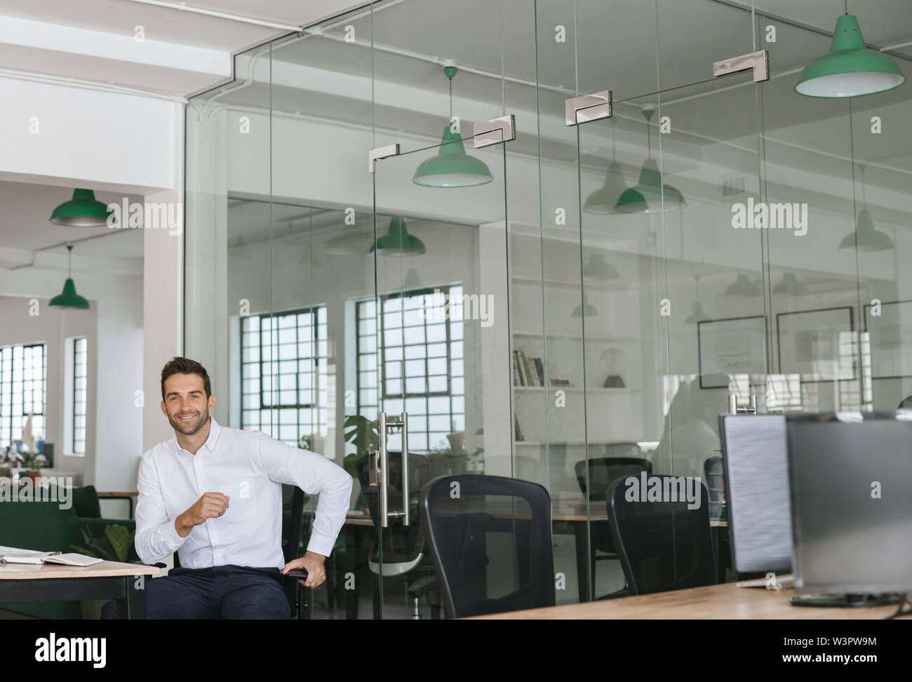 Smiling young businessman assis tout seul dans un grand bureau moderne Banque D'Images