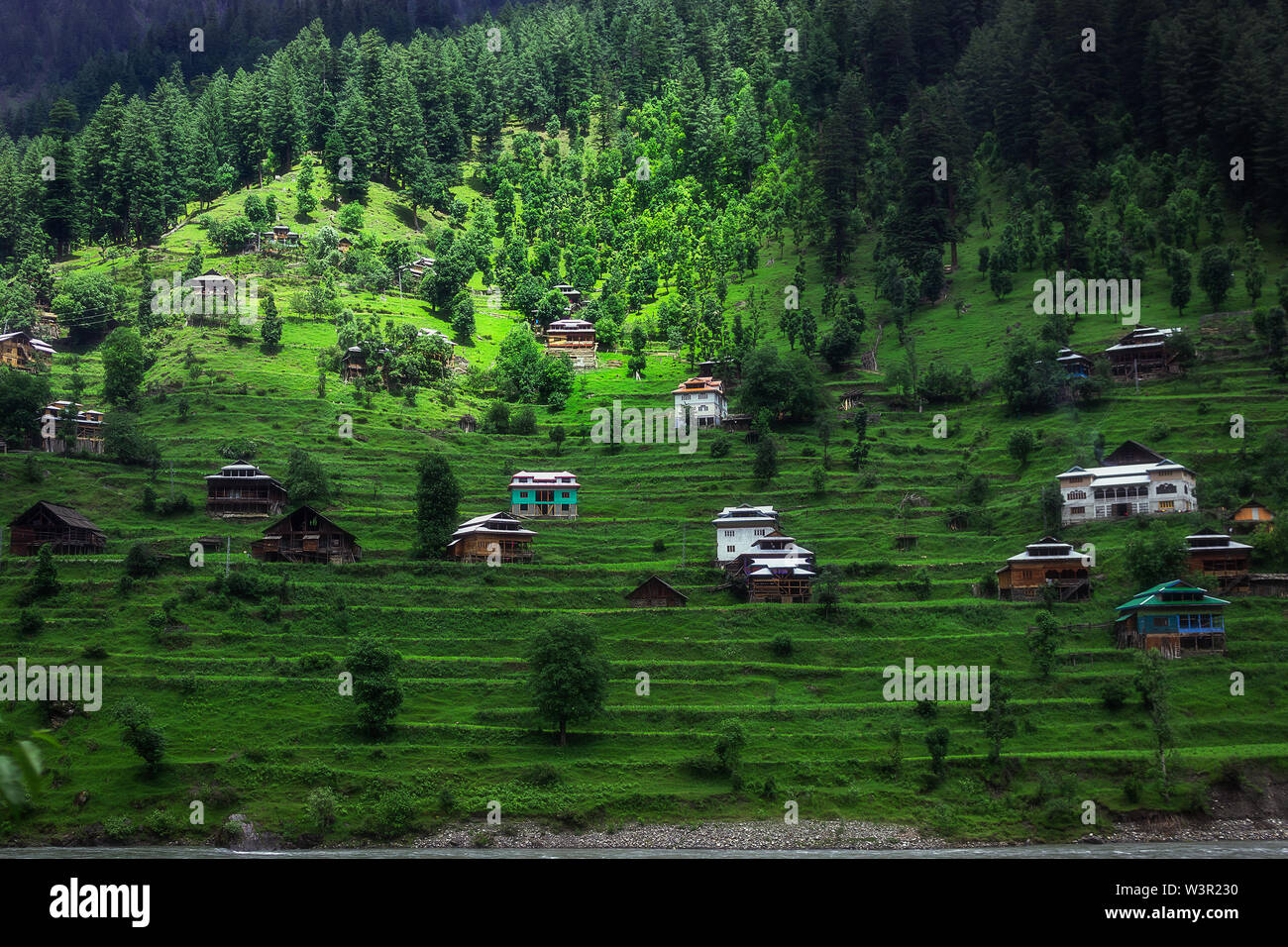 Un village rural avec des huttes dans une haute montagne verte avec des pics enneigés en arrière-plan dans le nord du Pakistan Banque D'Images