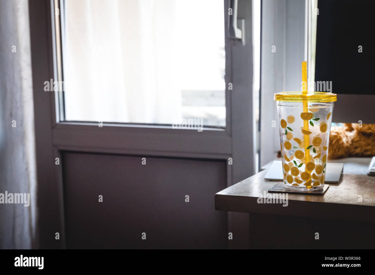 Un verre avec une paille avec citrons peint sur le bureau de l'office d'accueil près de l'ordinateur. Banque D'Images