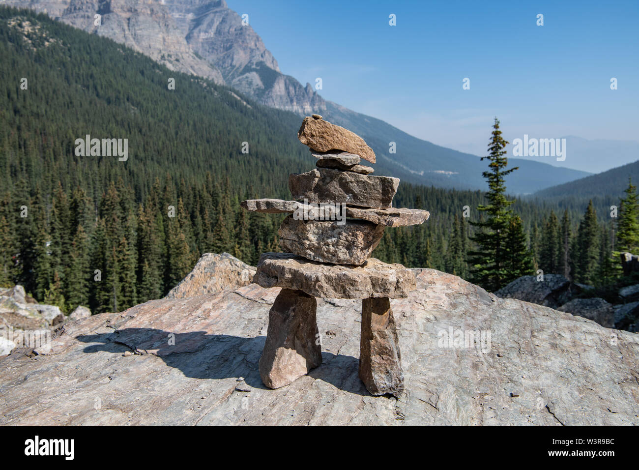La statue de pierre inspirée par Inuksuk se dresse contre une scène de forêt et de montagne au lac Moraine, Alberta, Canada Banque D'Images