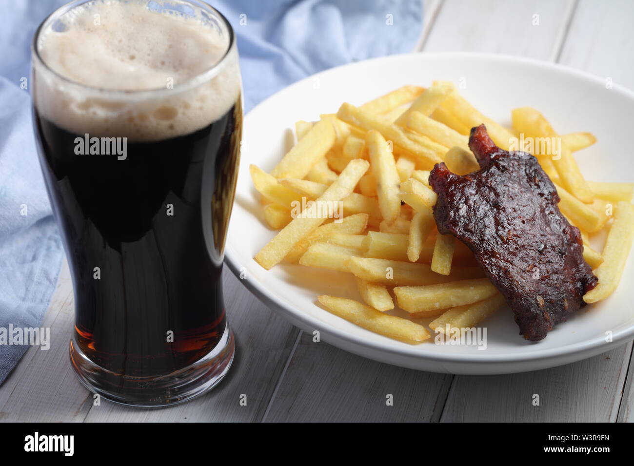 Côtes de porc grillées avec des frites et un verre de bière brune Banque D'Images
