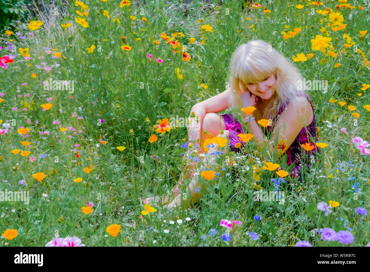 Blonde woman enjoying son jardin plein de fleurs sauvages. Remplacement de la pelouse. Banque D'Images