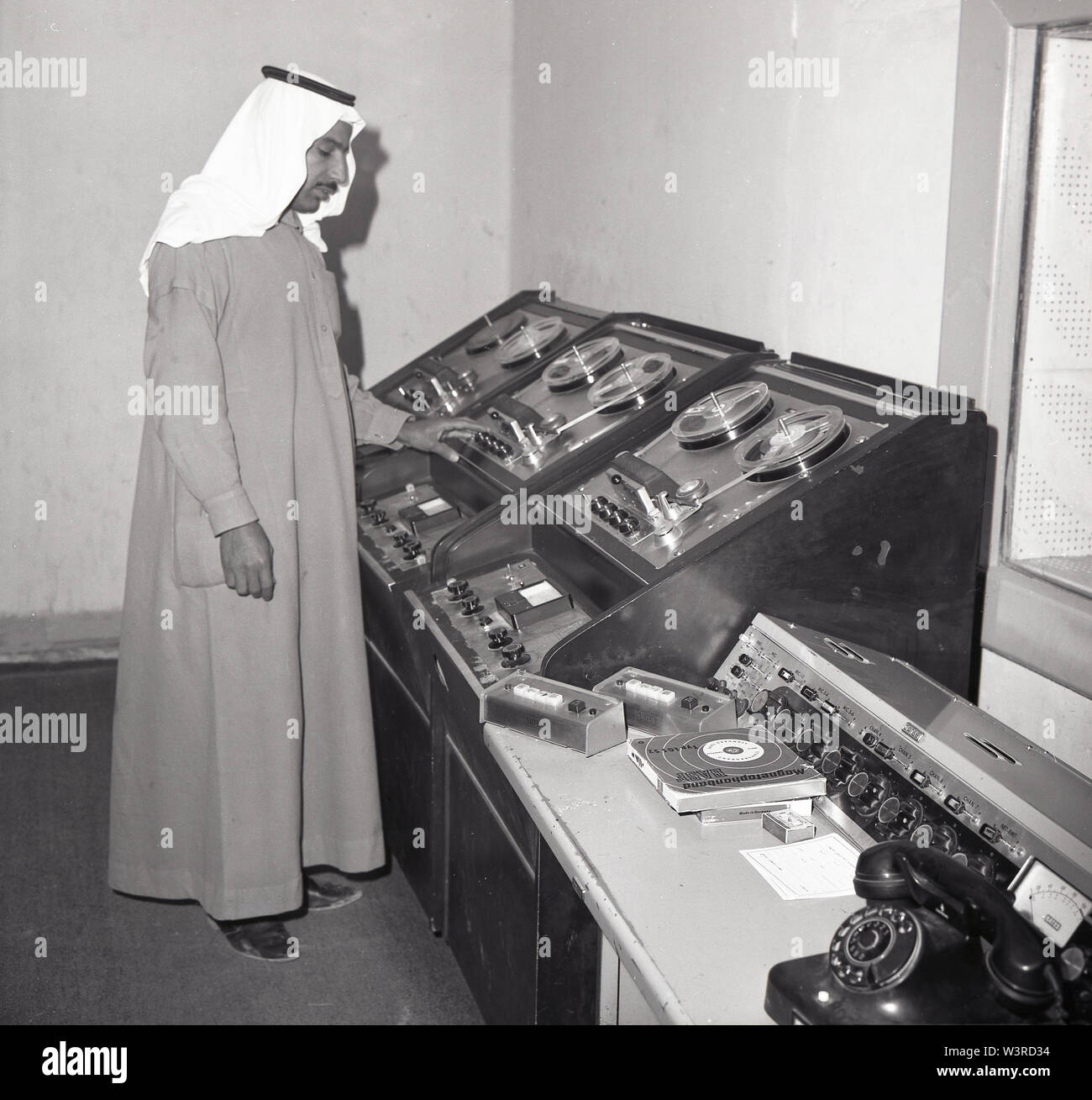 Années 1960, historique, un Arabe technicien studio portant un traditionnel à la cheville d'un garnent Thawb ou Thobe et coiffure, un keffieh, travaillant à un magnétophone dans une émission de télévision, l'Arabie Saoudite. Banque D'Images