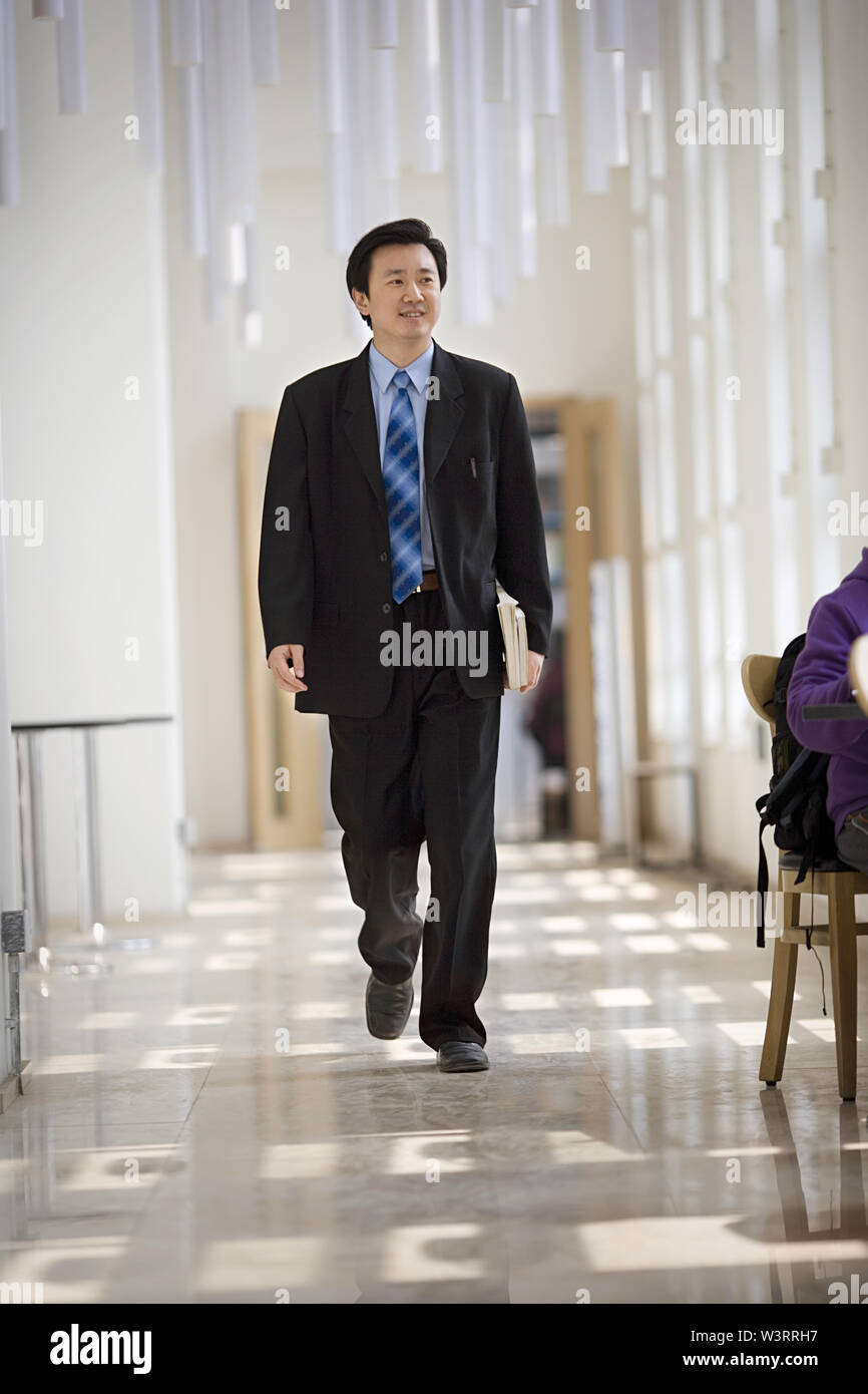 Mid-adult male teacher marcher le long d'un hall d'une école. Banque D'Images
